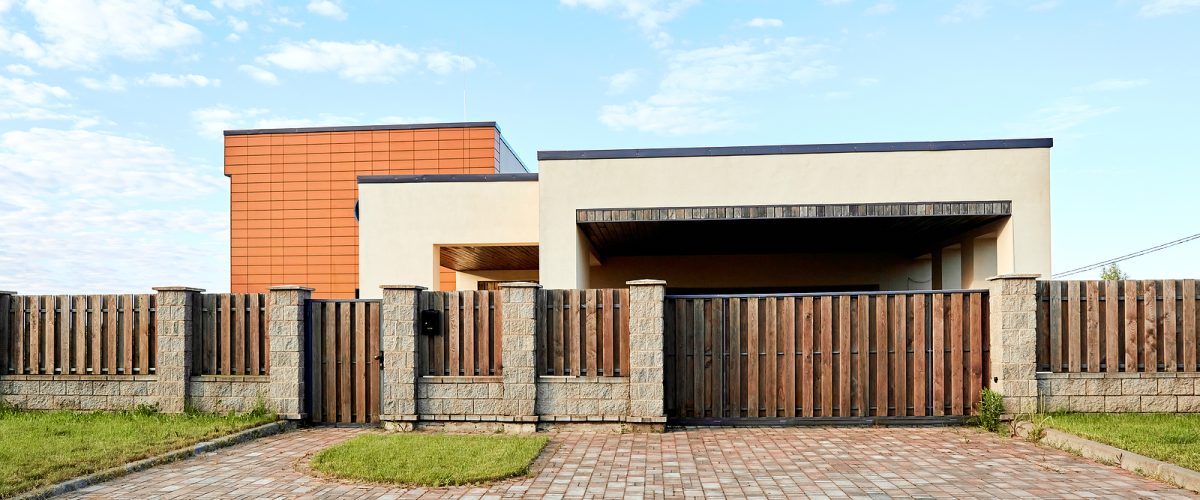 Brown metal profile fence with block posts. Incline construction. Corrugated surface. Security. Private property fencing. Opaque hedge. Outdoor house exterior. Side view. Urban or industrial style.