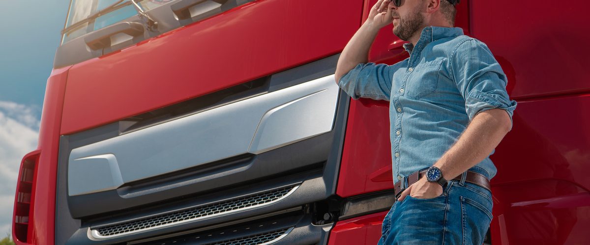 Caucasian Euro Semi Truck Driver in Front of His Brand New Red Truck Tractor. Automotive and Heavy Duty Transportation Industry Theme.