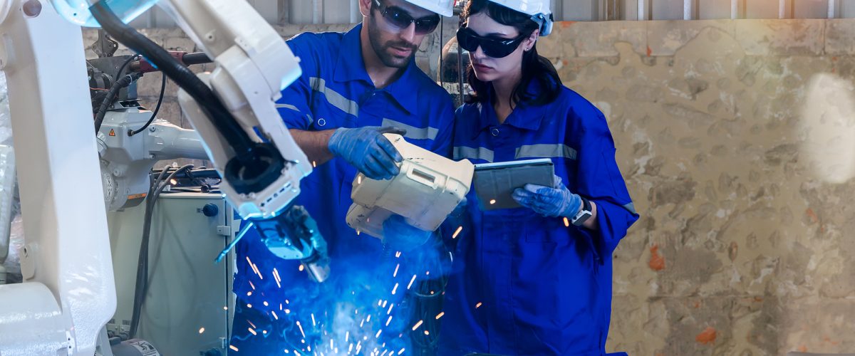 Male and female engineers and industrial electronics technicians holding remote control electric welding robot arm for complete welding trial work in robotic assembly plant to inspect applications.