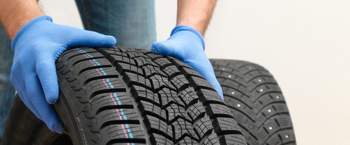 Mechanic holding a tire at the repair garage. Replacement of winter and summer tires. winter studded tyre, tires replacement