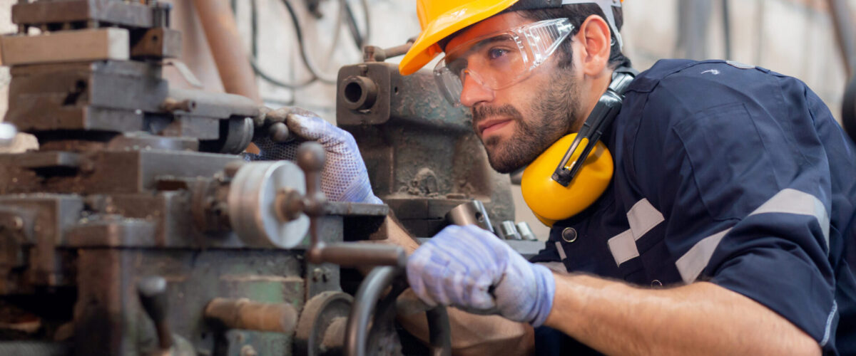 Young caucasian engineer man operating lathe machine for preparing production at factory industrial, technician or labor maintenance machinery at workplace, metalworker working, industry concept.